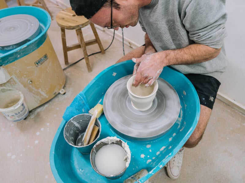 Man sitting at a pottery wheel spinning clay into a bowl